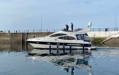 A white and blue motor yacht, equipped with a sleek boat mooring hook, navigates a harbor with two people on the deck.