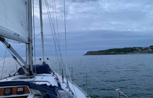 View from the deck of a sailboat on calm waters, with distant land and cloudy sky in the background, as a buoy catcher gently drifts by.
