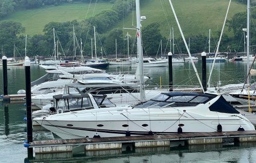 Several yachts docked at a marina, with a backdrop of green hills and trees, where boat mooring hooks are poised for swift securing.